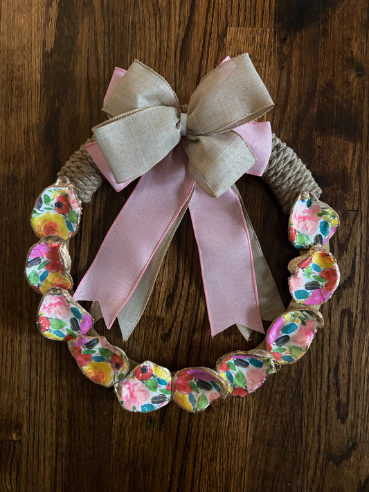 Decorative wreath with floral pattern, pink ribbon, and beige bow on a wooden surface