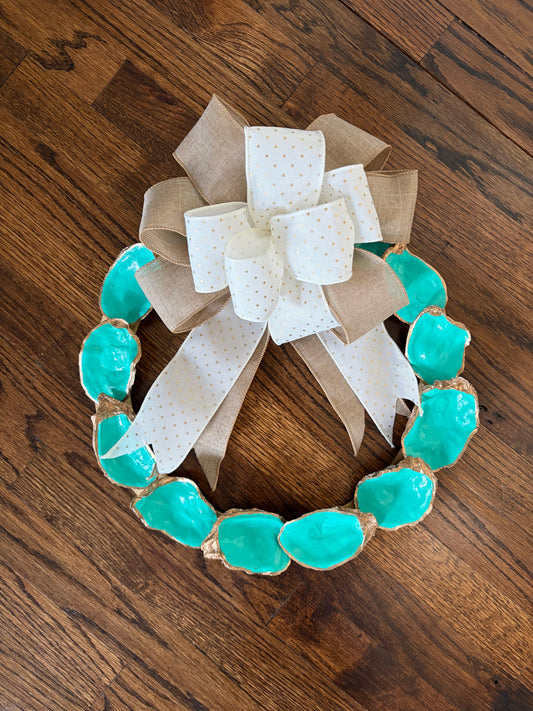 Decorative wreath with turquoise oyster shells and a large bow on a wooden surface